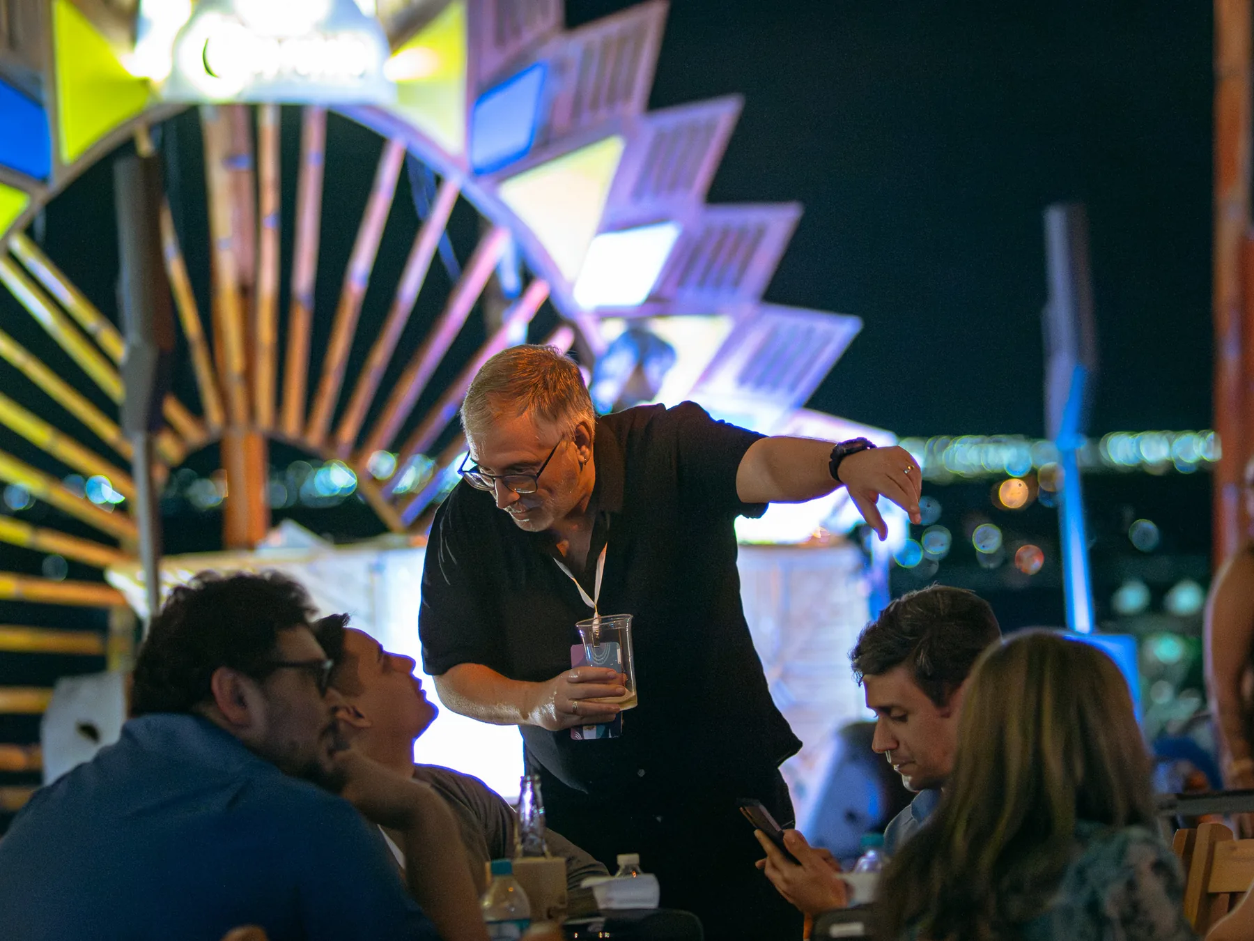 Convidados nas mesas do deck com o palco iluminado ao fundo
