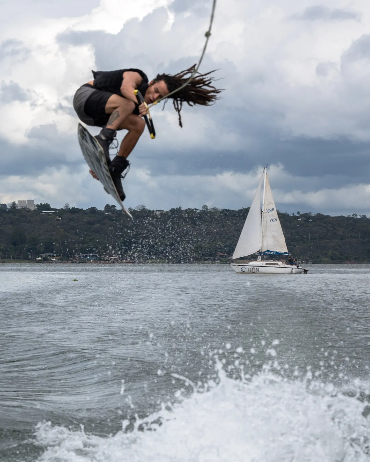 Aéreo de wakeboard com veleiro ao fundo no Lago Paranoá